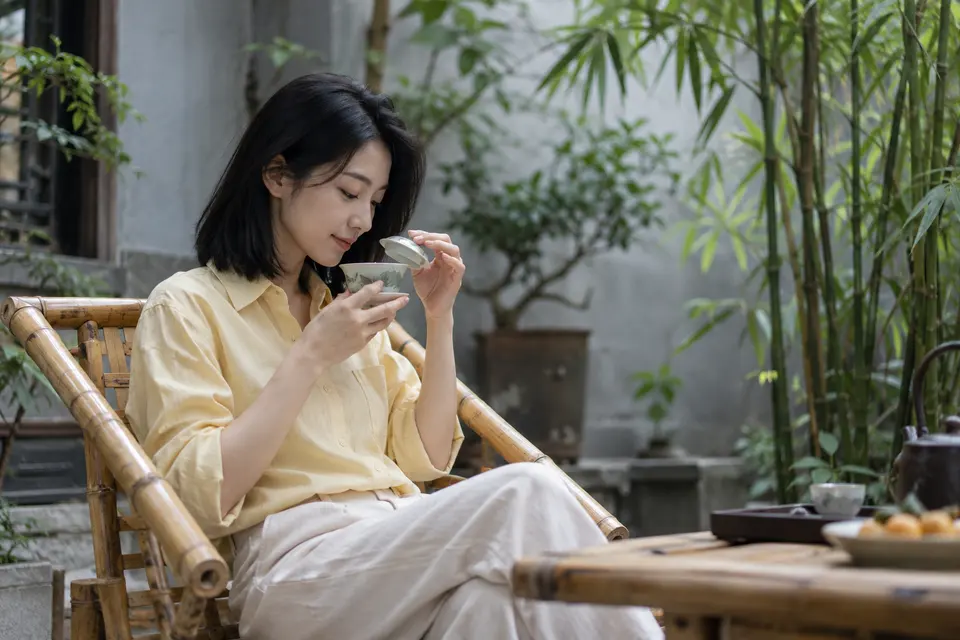 竹影庭院中，年轻女性端起盖碗闻香